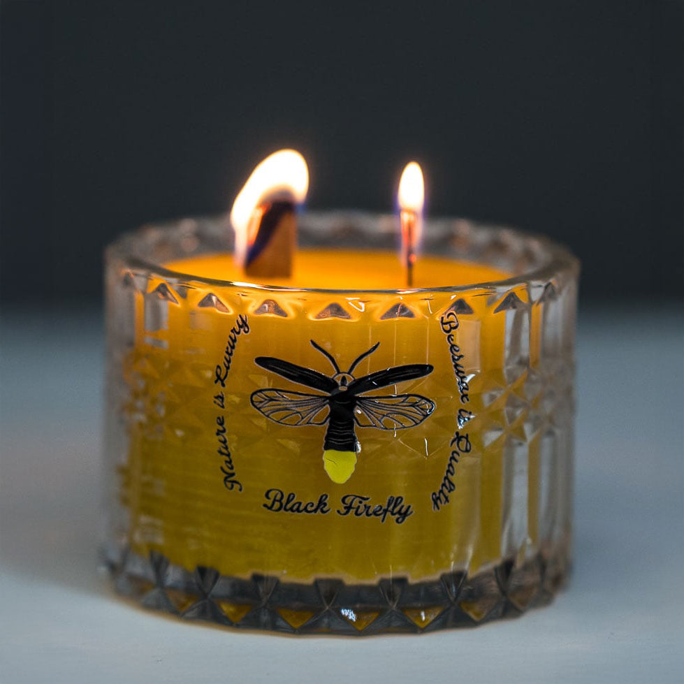 Candle in a glass holder with a label featuring a black firefly design on a dark background.