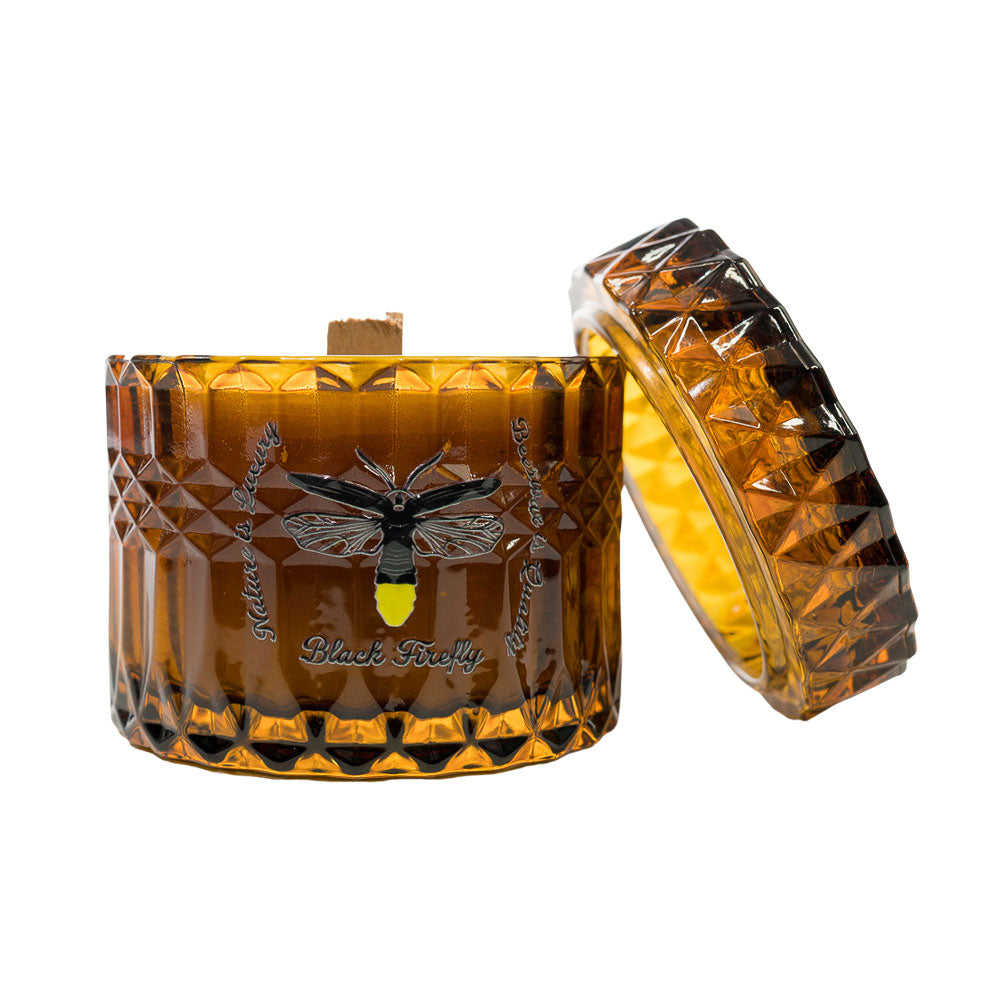 Amber glass candle with decorative lid featuring a bee design on a white background